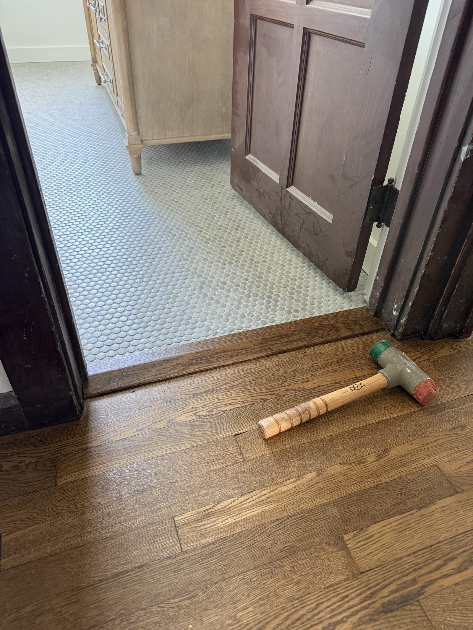 Hardwood plank hallway floor leading to a tiled bathroom doorway