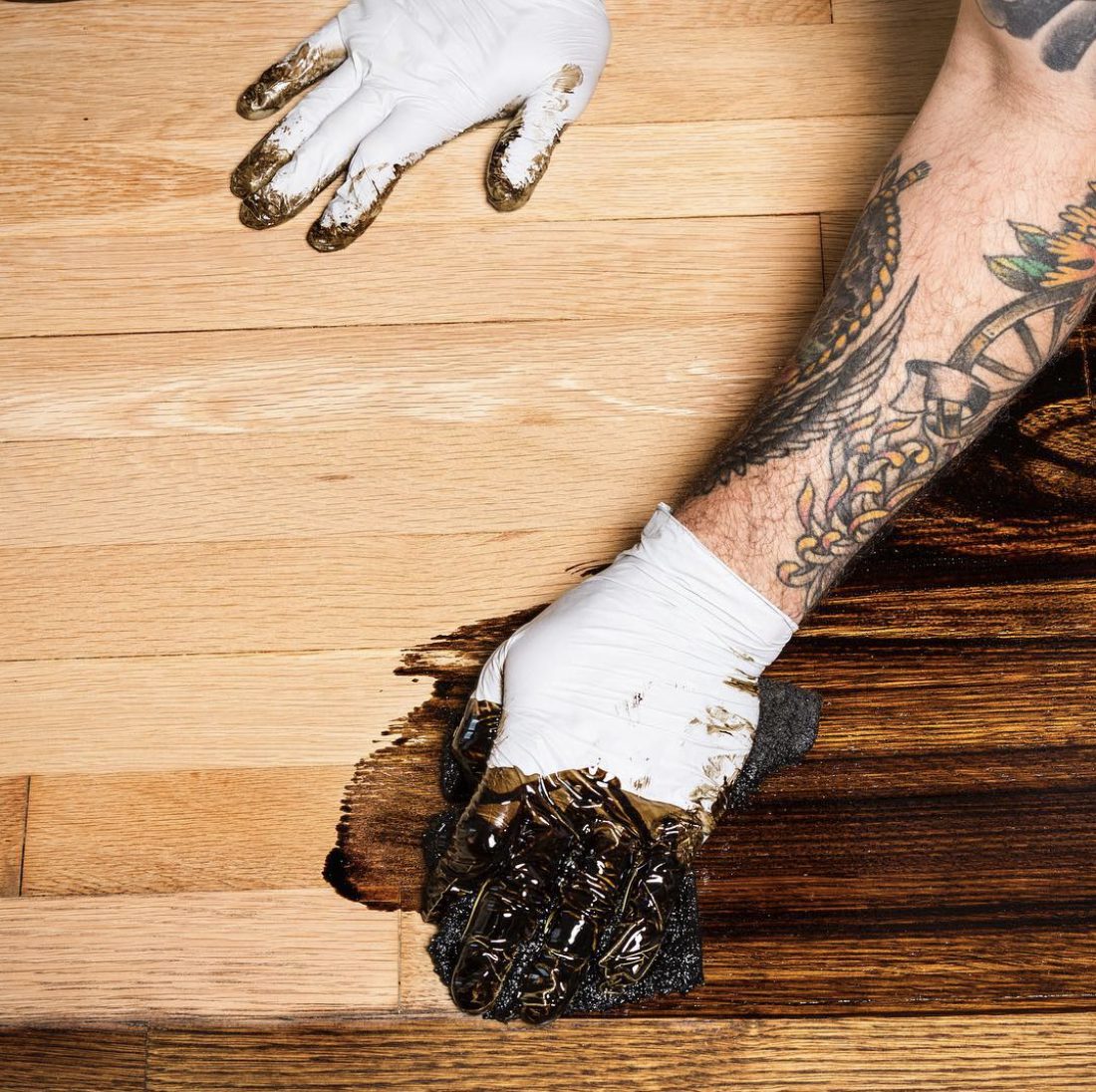 Hand applying wood stain to a hardwood floor during refinishing